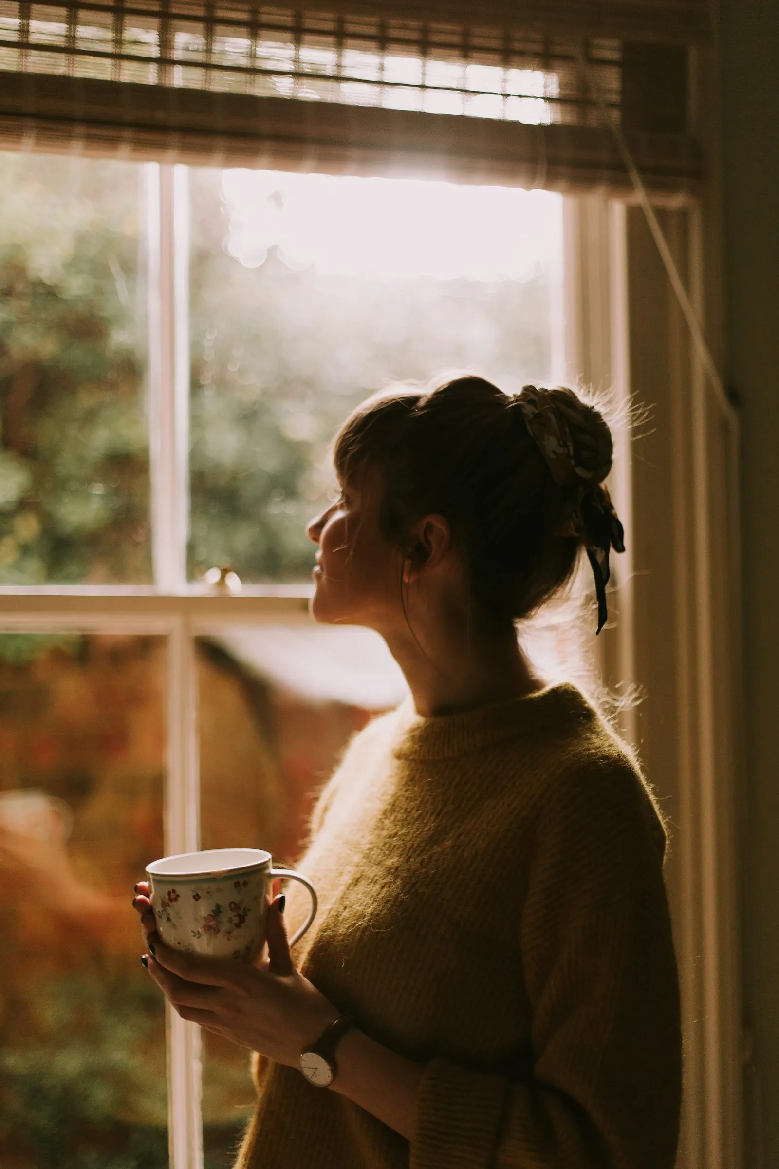 Mujer de espaldas mirando por una ventana iluminada por el sol